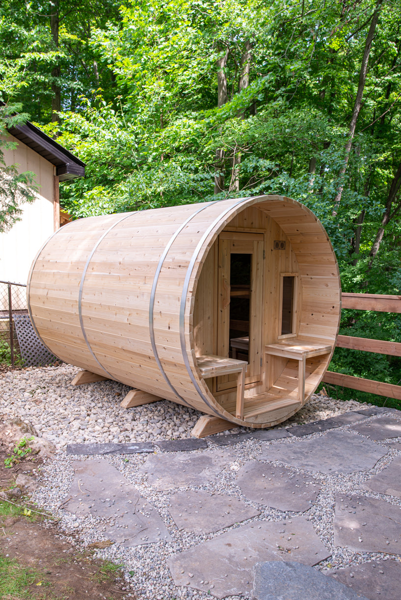 Dundalk CT Tranquility 6-Person Outdoor Barrel Sauna with porch bench on a stone patio