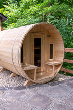 Front view of the Dundalk CT Tranquility 6-Person Outdoor Barrel Sauna with porch bench and trees