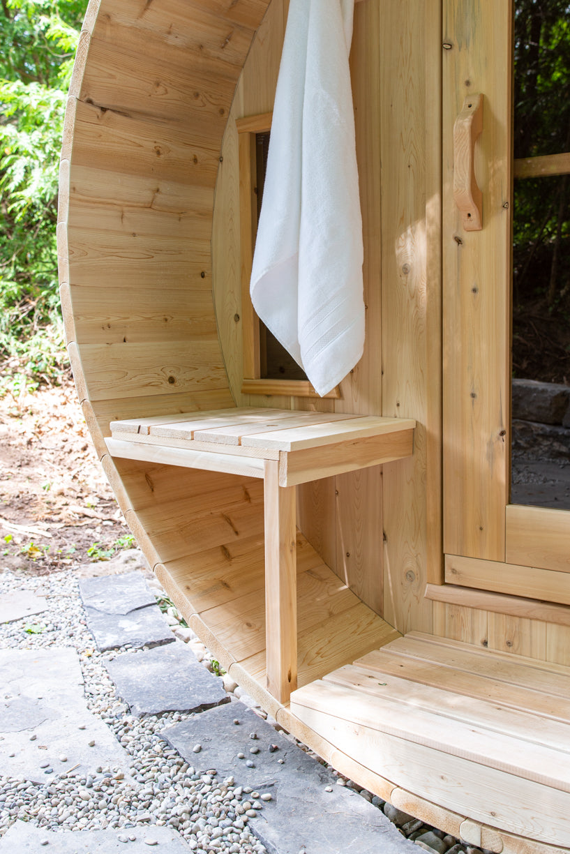 Porch bench and towel at the door of the Dundalk CT Tranquility 6-Person Outdoor Barrel Sauna