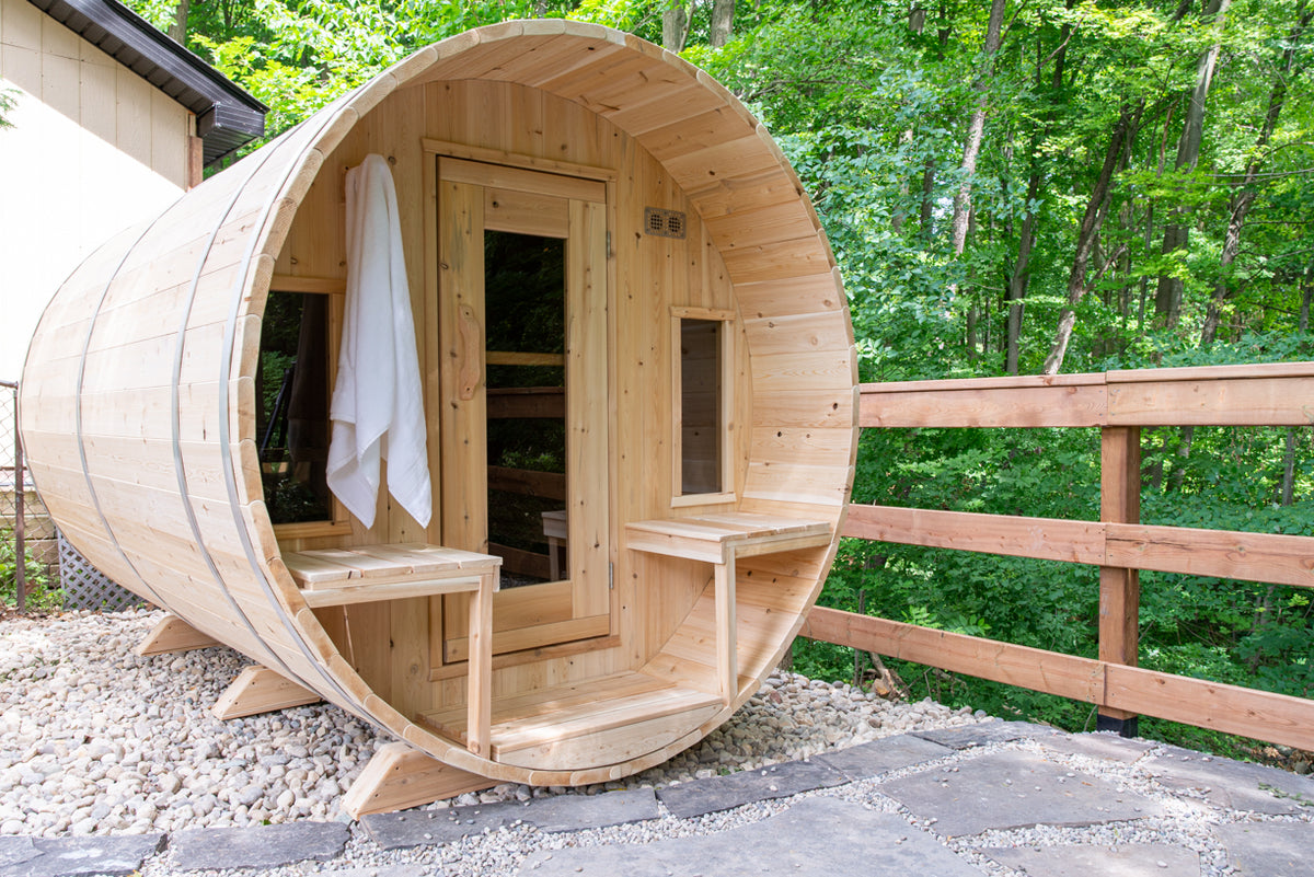 Front view of the Dundalk CT Tranquility 6-Person Outdoor Barrel Sauna beside a wooden fence