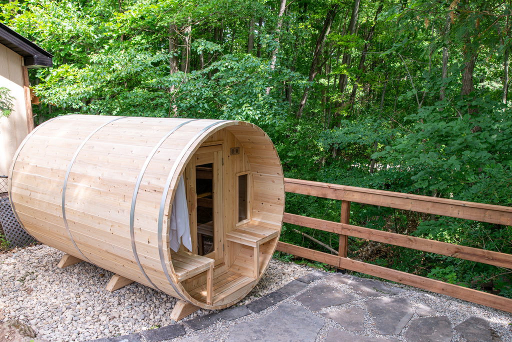 Angled view of the Dundalk CT Tranquility 6-Person Outdoor Barrel Sauna beside a wooden fence