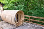 Angled view of the Dundalk CT Tranquility 6-Person Outdoor Barrel Sauna beside a wooden fence