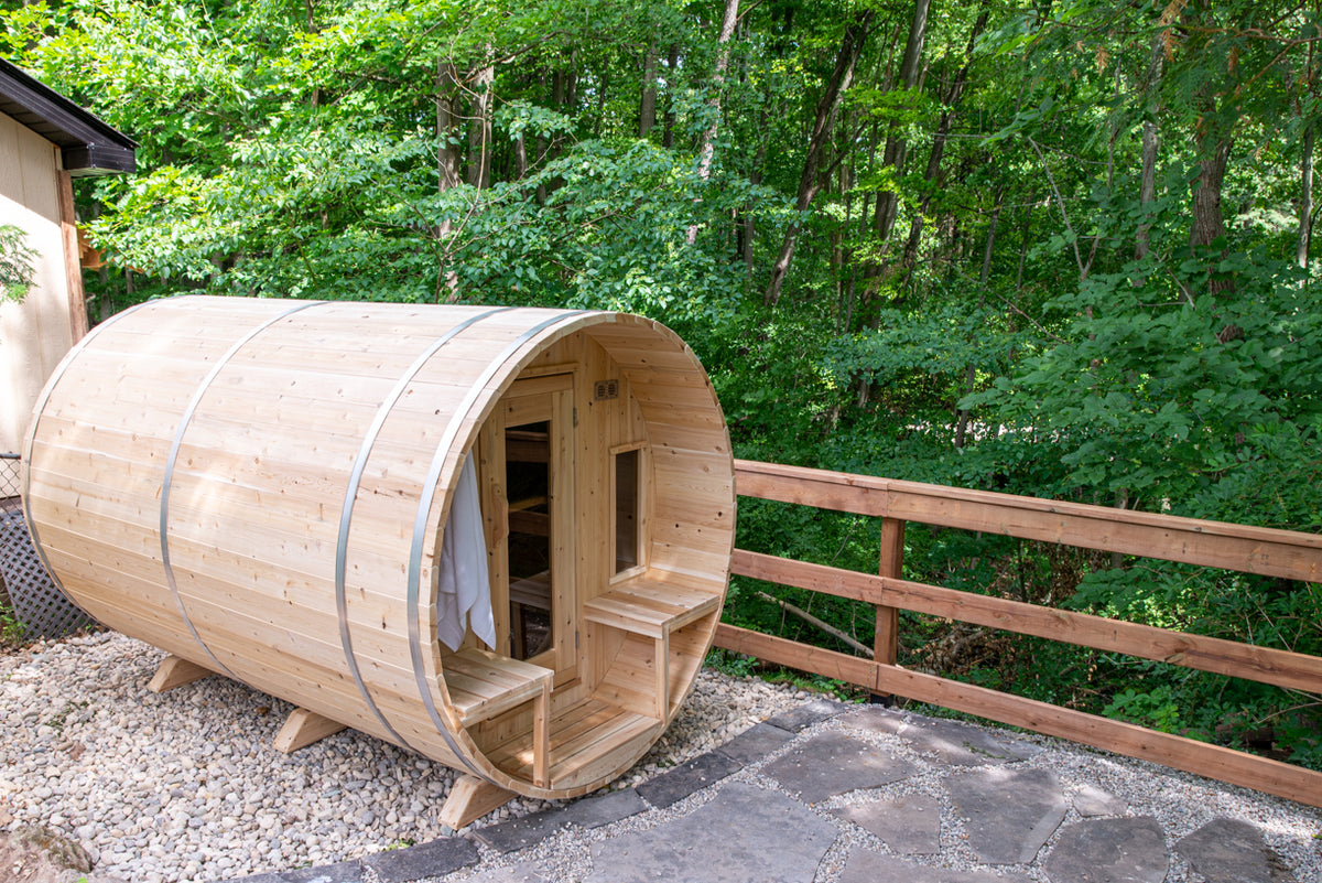 Angled view of the Dundalk CT Tranquility 6-Person Outdoor Barrel Sauna beside a wooden fence