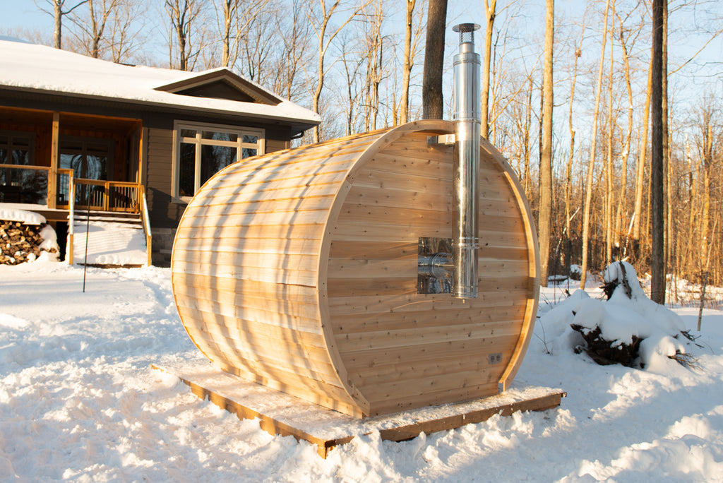 Side view of the Dundalk CT Elation 4-Person Outdoor Barrel Sauna with a house in the background in winter