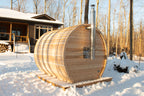 Side view of the Dundalk CT Elation 4-Person Outdoor Barrel Sauna with a house in the background in winter