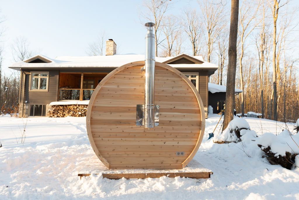 Rear view of the Dundalk CT Elation 4-Person Outdoor Barrel Sauna with stove chimney pipe in winter