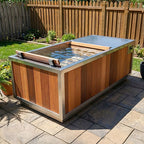 Finnmark SoulCold plunge tub filled with water on a stone patio, with cedar backrest