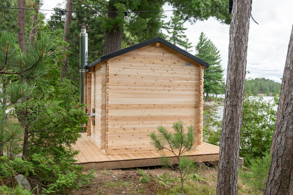 Side view of the Dundalk CT Georgian 6-Person Outdoor Cabin Sauna among pine trees