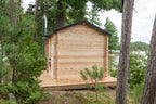 Side view of the Dundalk CT Georgian 6-Person Outdoor Cabin Sauna among pine trees