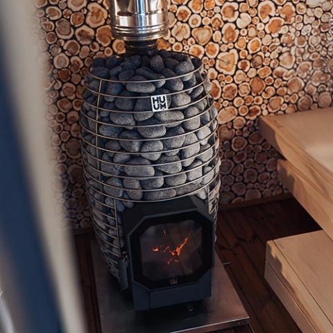 Huum Hive Flow Mini 8.5kW wood-burning sauna stove installed in a sauna with stones and wooden benches