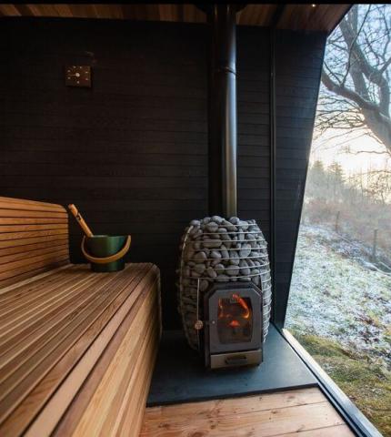 Huum Hive Wood 13kW wood-burning sauna stove installed in a sauna with chimney pipe beside the bench
