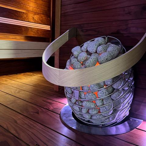 Huum Drop 6kW Sauna Heater in a sauna with curved wooden safety rail and floor plate