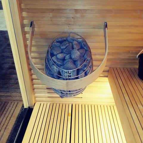 Huum Drop 7.5kW Sauna Heater in a sauna with safety rail and warm lighting