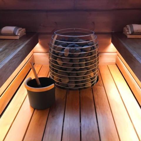 Huum Hive 15kW Sauna Heater in a sauna with bucket and ladle on lit benches