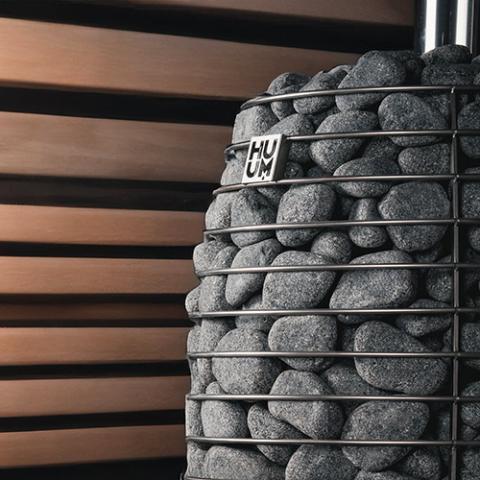 Huum Hive Flow LS 9.8kW wood-burning sauna stove with sauna stones beside a slatted wood sauna wall