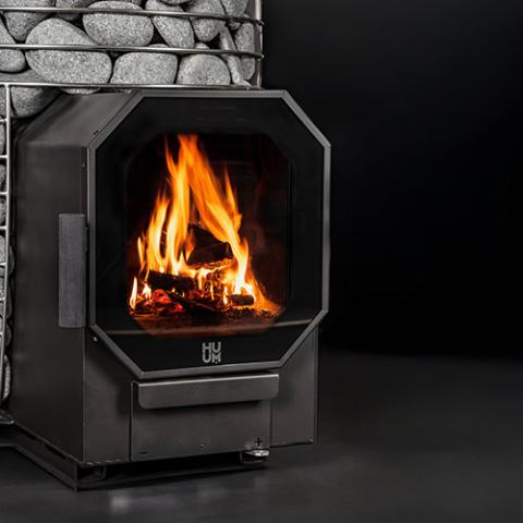 Close-up of the glass fire door with flames burning on the Huum Hive Flow Mini LS 8.5kW wood-burning sauna stove