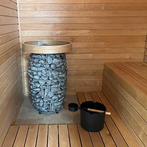 Huum Hive Mini 10.6kW electric sauna heater in a sauna with bucket and ladle