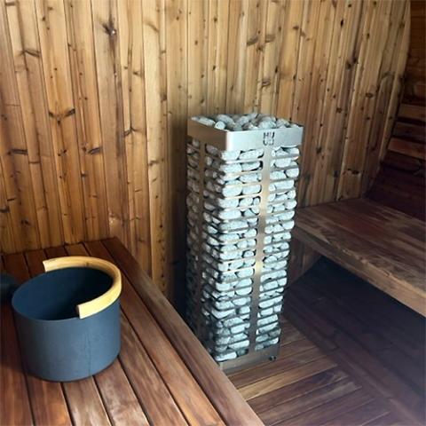 Huum Steel 10.5kW Sauna Heater in a wood-panelled sauna next to a bucket