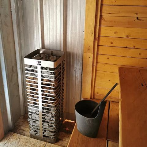 Huum Steel 6kW Sauna Heater in a sauna beside a bucket and ladle