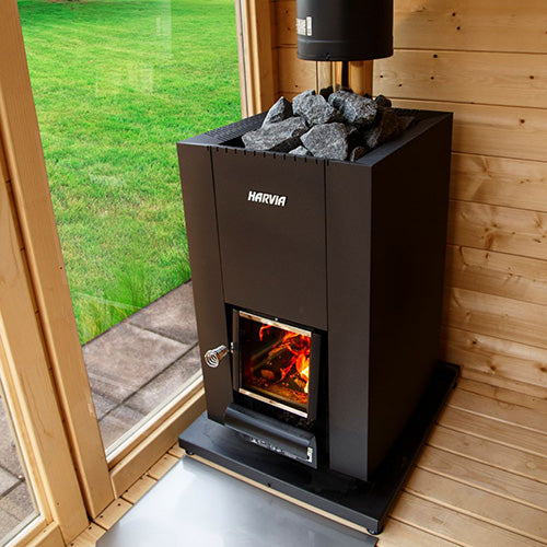 Harvia Linear 18 Compact 14.3kW Wood-Burning Sauna Stove installed in a sauna beside a glass wall with garden view