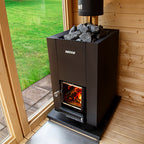 Harvia Linear 18 Compact 14.3kW Wood-Burning Sauna Stove installed in a sauna beside a glass wall with garden view
