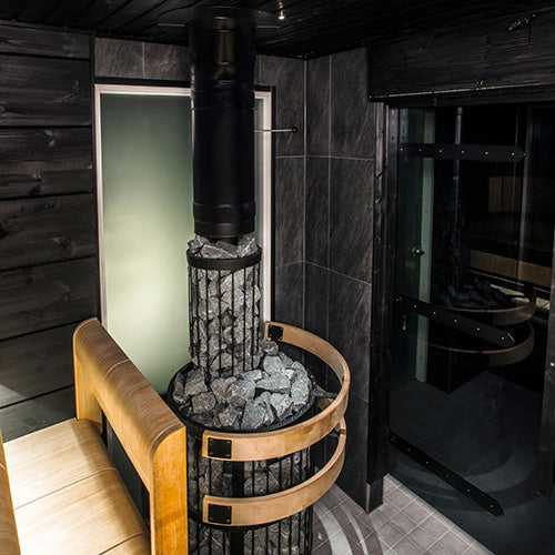 Harvia Legend 240 Duo 21kW Wood-Burning Sauna Stove and Fireplace installed in a dark sauna with chimney pipe and stone ring