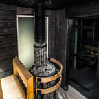 Harvia Legend 240 Duo 21kW Wood-Burning Sauna Stove and Fireplace installed in a dark sauna with chimney pipe and stone ring