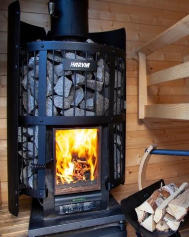 Harvia Legend 240 GreenFlame 15.9kW Wood-Burning Sauna Stove with fire burning and firewood beside it in a sauna