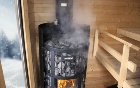Harvia Legend 240 GreenFlame 15.9kW Wood-Burning Sauna Stove in a sauna with steam rising and a snowy window view