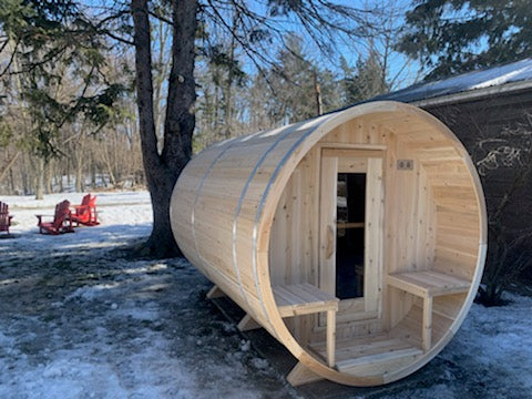 Side view of the Dundalk CT Serenity 5-Person Outdoor Barrel Sauna among trees in winter