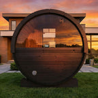 SaunaLife E6 Ergo 3-person outdoor barrel sauna with panoramic window at sunset in front of a modern house
